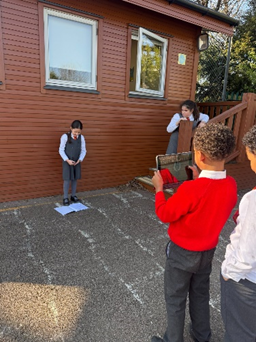 A child standing a reporting on the process of digestion whilst another child records them with an iPad.  