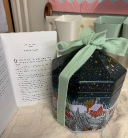 A tin of Turkish Delight wrapped in a green ribbon with the first page of Chapter 4 open next to it.   