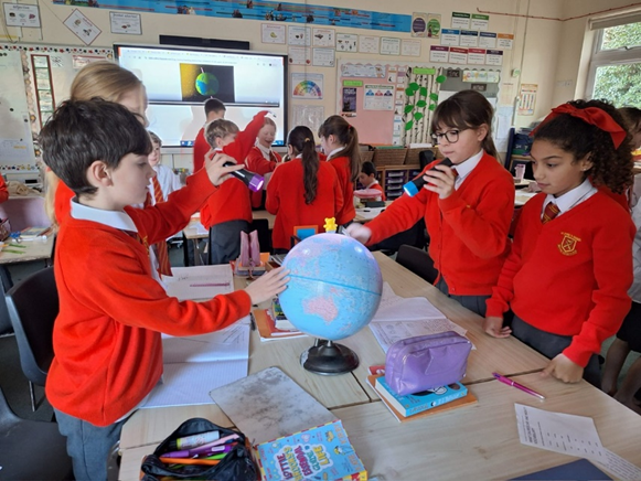 Children rotating a globe in a small group using a torch and figure to explain day and night.