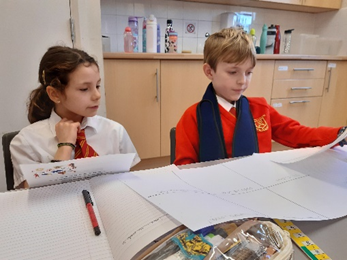 Two children gathered around a guided reading text reading information about plastics.  