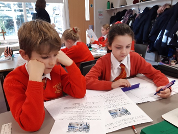 Two children gathered around a guided reading text. One child is writing down the information they have gathered. 