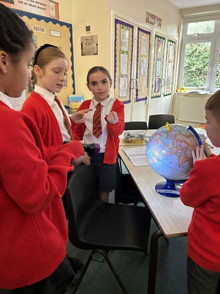 Children rotating a globe in a small group. Two children are explaining the concept to another.